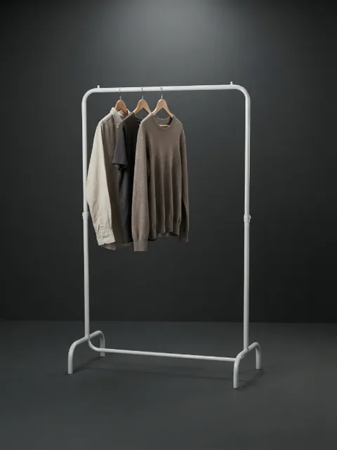 Arara de roupa branca dobrável de uma barra, com três camisas em tons neutros, fotografada em estúdio sobre fundo dourado